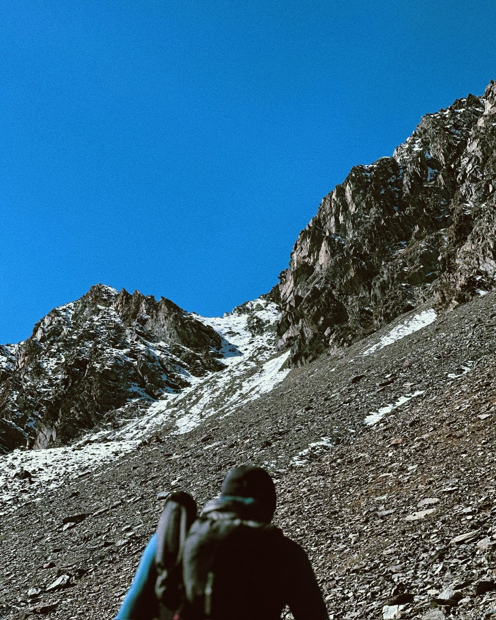 A runner looking up a steep scree slope towards rocky, snow-streaked peaks
