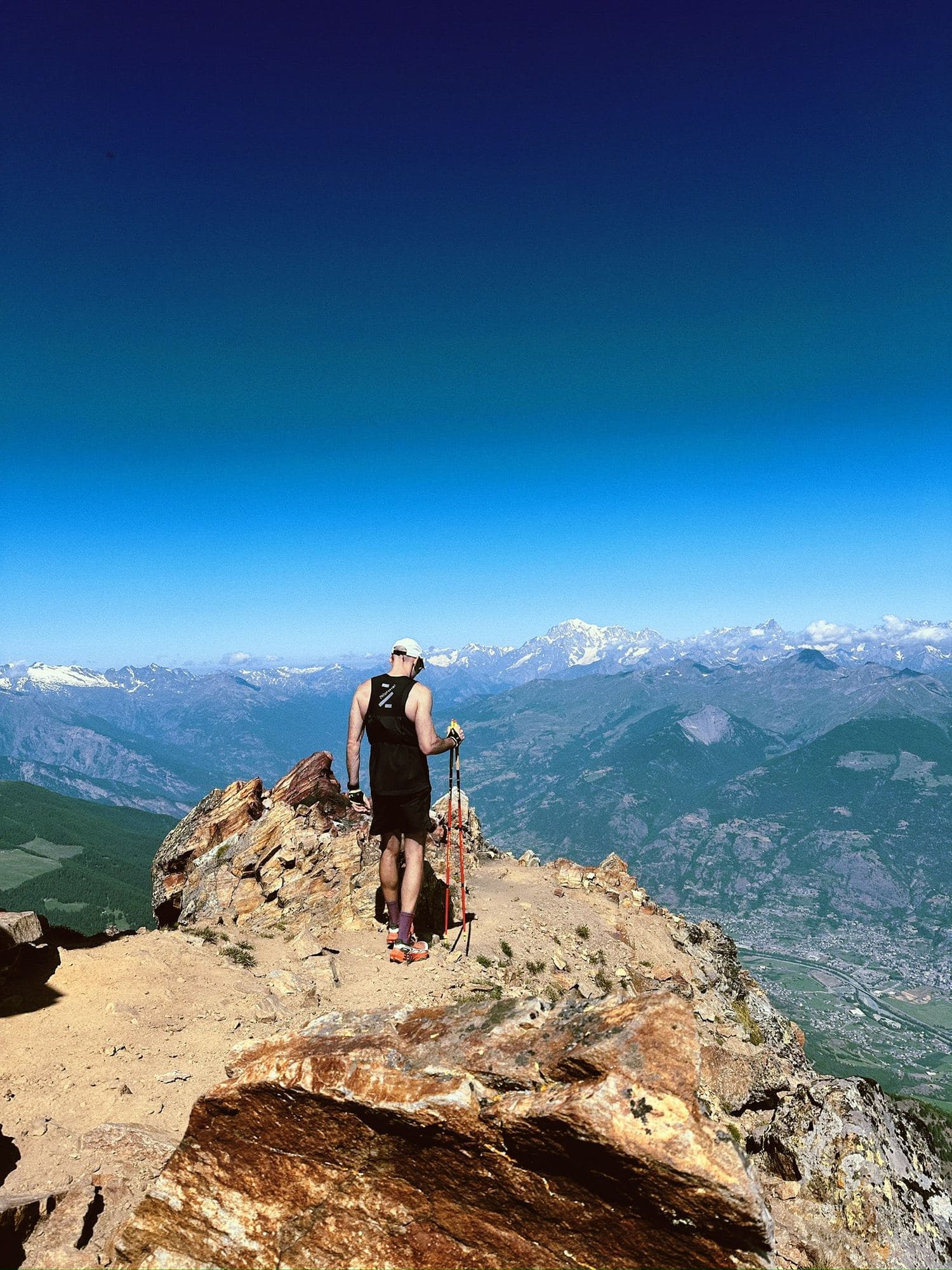 A runner with poles on a rocky summit above a valley