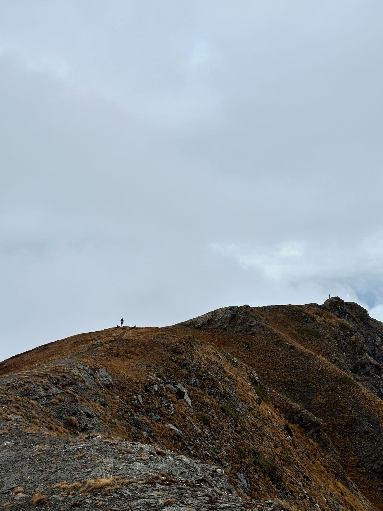 Two runners small on a mountain ridge under a grey sky