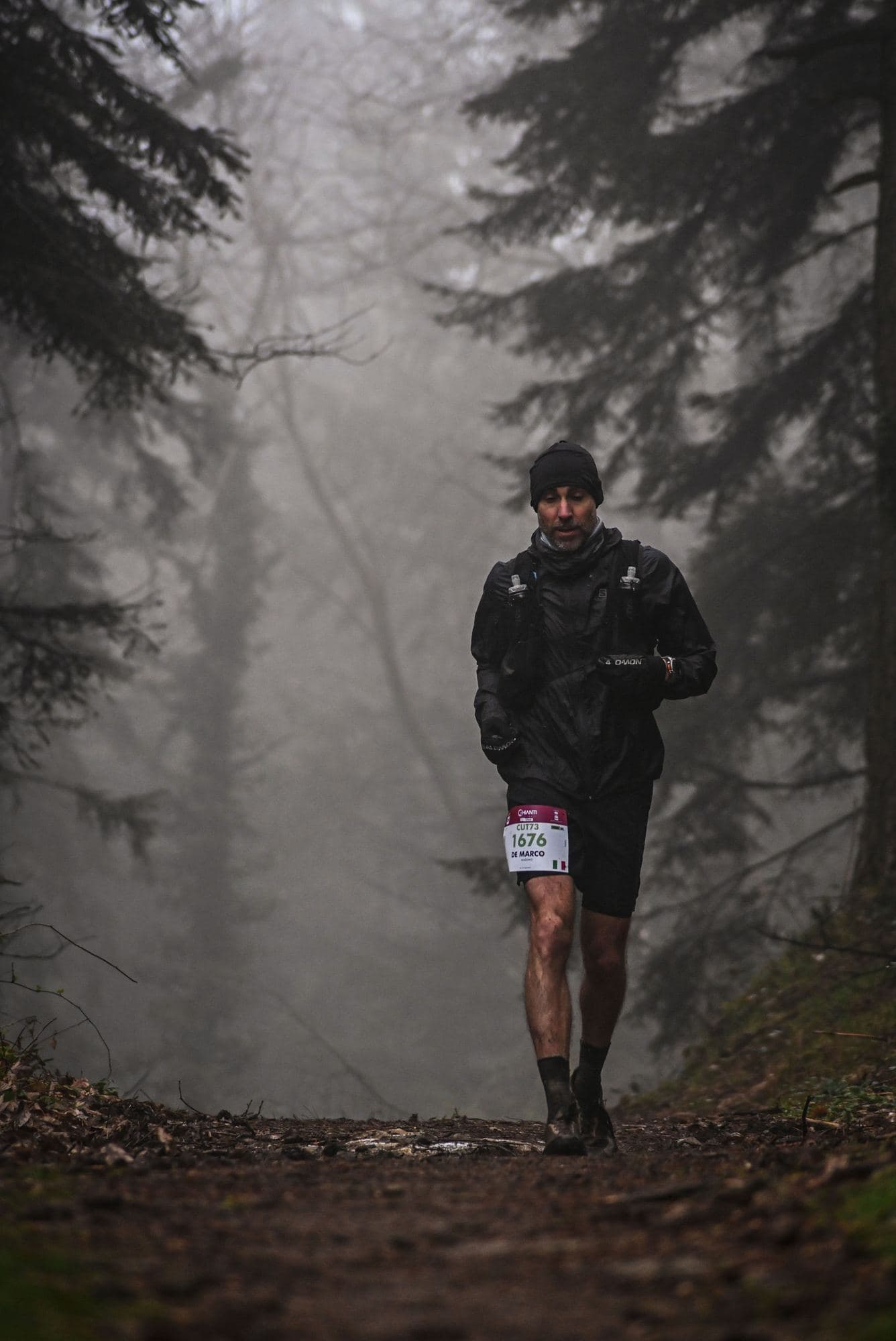 A runner with a race bib coming down a forest trail in the fog