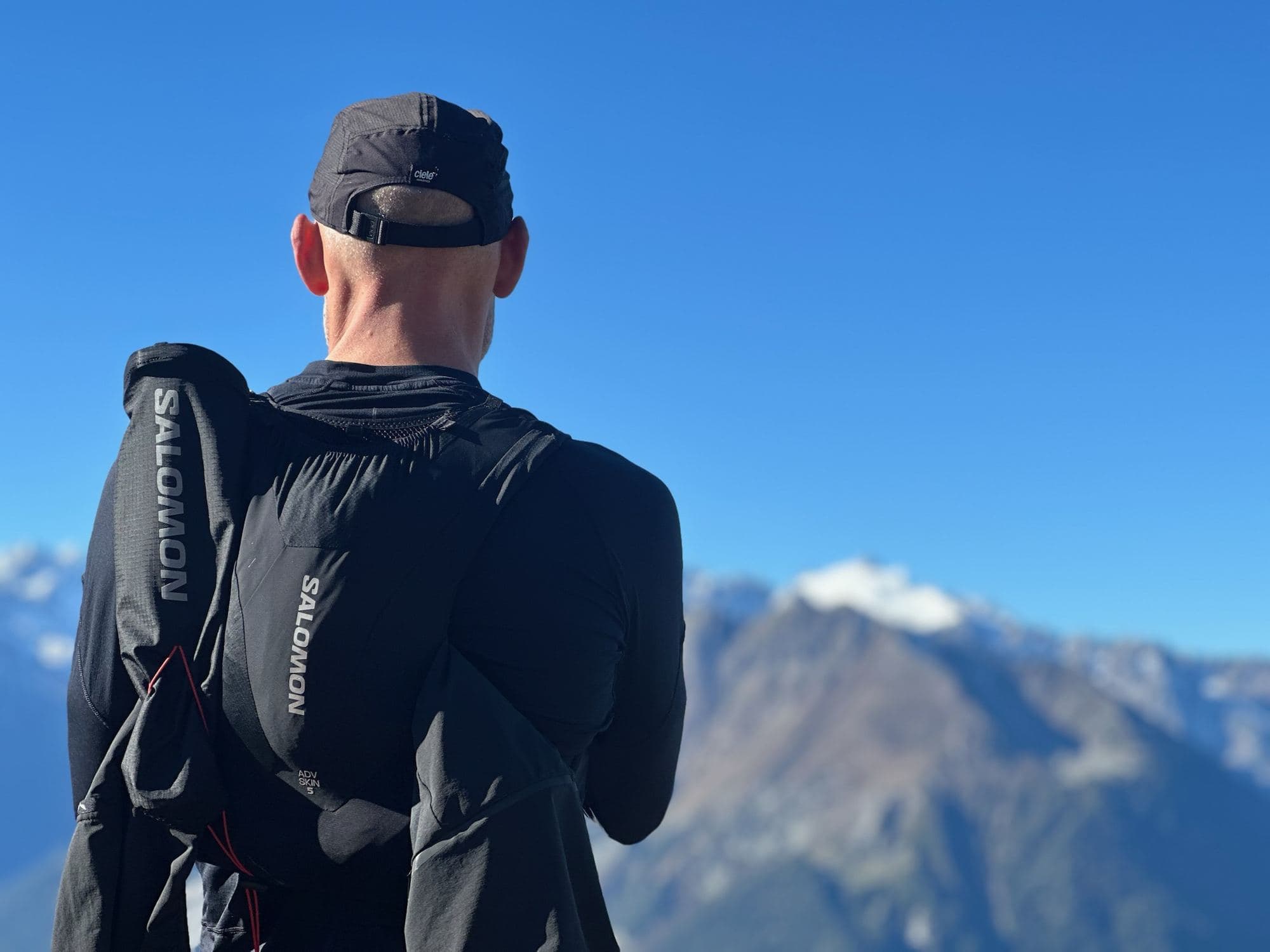 A runner in a race vest looking out at snow-capped mountains